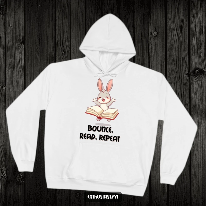 Funny hoodie depicting a joyful bunny bouncing with a large, open book, perfect for cozy reading sessions.
